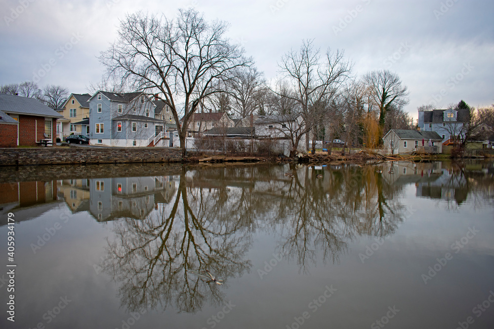 Reflections of barren trees and houses in the still waters of Peddie lake in Hightstown, New Jersey, on a cloudy afternoon -01