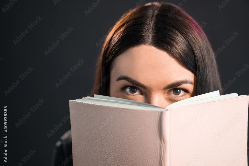 Beautiful brunette girl looking from behing the book in pink cover. Beautiful brunette girl looking from behing the book in pink cover.