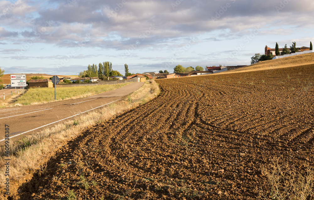 a paved road on a plowed field entering Ledigos village, province of Palencia, Castile and Leon, Spain