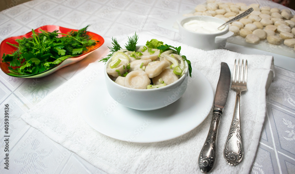 Bowl of cooked homemade dumplings garnished with green dill and parsley leaves with a fork and knife.