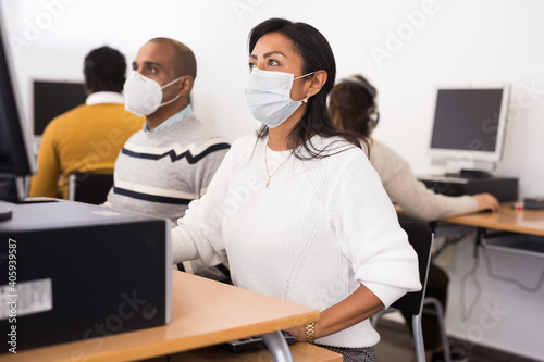Adult hispanic woman in protective face mask sitting at table with computer and books  studying in library. New normal in coronavirus pandemic