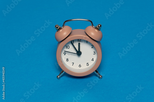 Brown alarm retro clock on blue background. Five minutes to twelve. Creative time concept