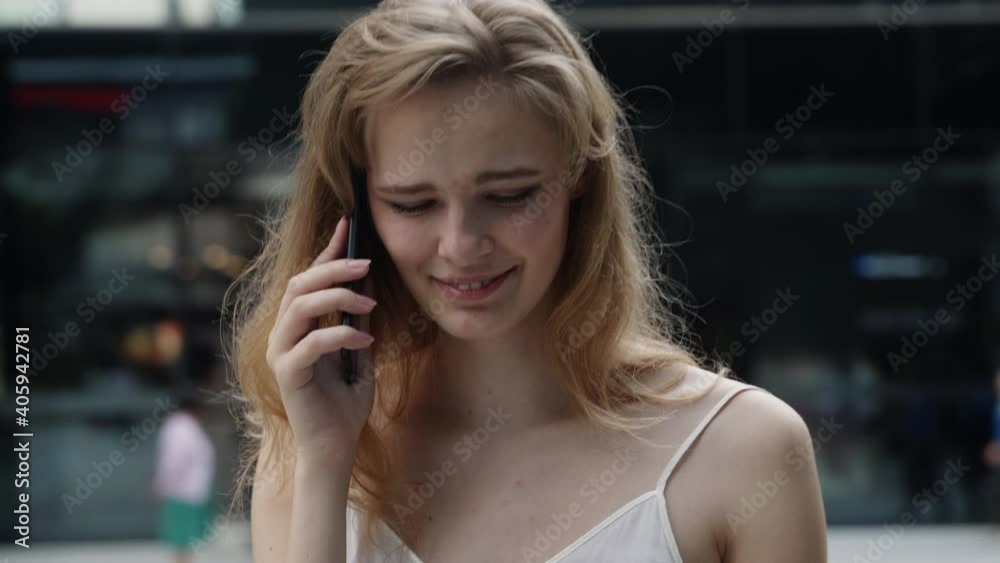 Young business woman in a white t-shirt is laughs and talking on the phone with business partners or friends with a business center or shopping mall behind. Happy girl tells or hears something funny. Young business woman in a white t-shirt is laughs and talking on the phone with business partners or friends with a business center or shopping mall behind. Happy girl tells or hears something funny.