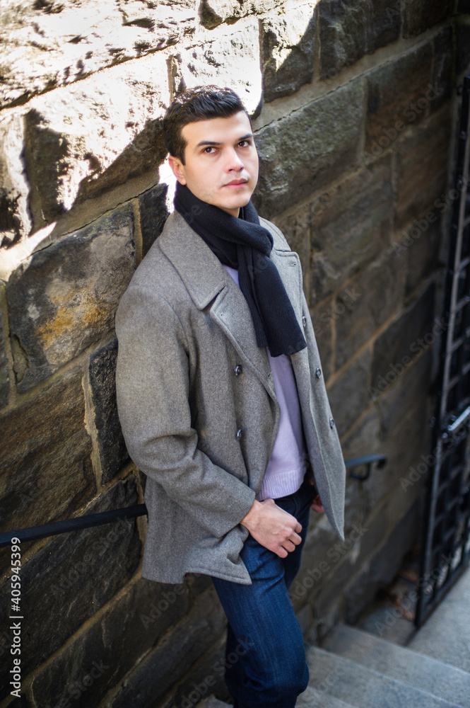 A young guy is standing by a wall, hopefully looking up.