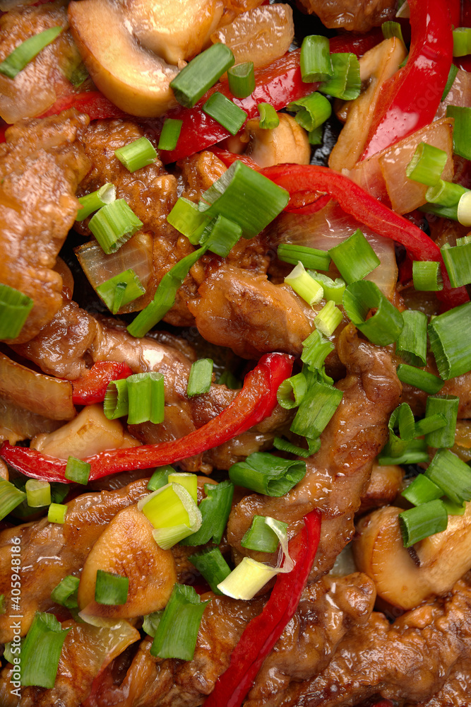 Fried meat with vegetables, green onions, bell peppers and mushrooms, in a frying pan, on a wooden background Fried meat with vegetables, green onions, bell peppers and mushrooms, in a frying pan, on a wooden background
