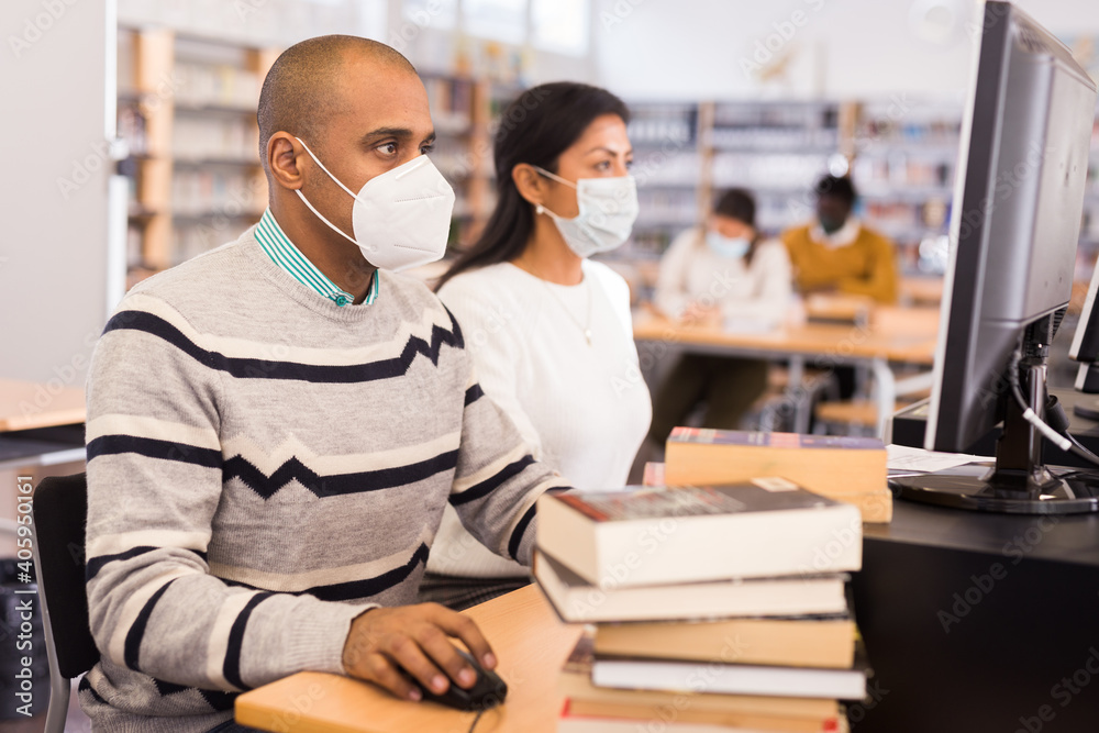 Portrait of hispanic man in protective mask studying in computer class in public library during coronavirus pandemic