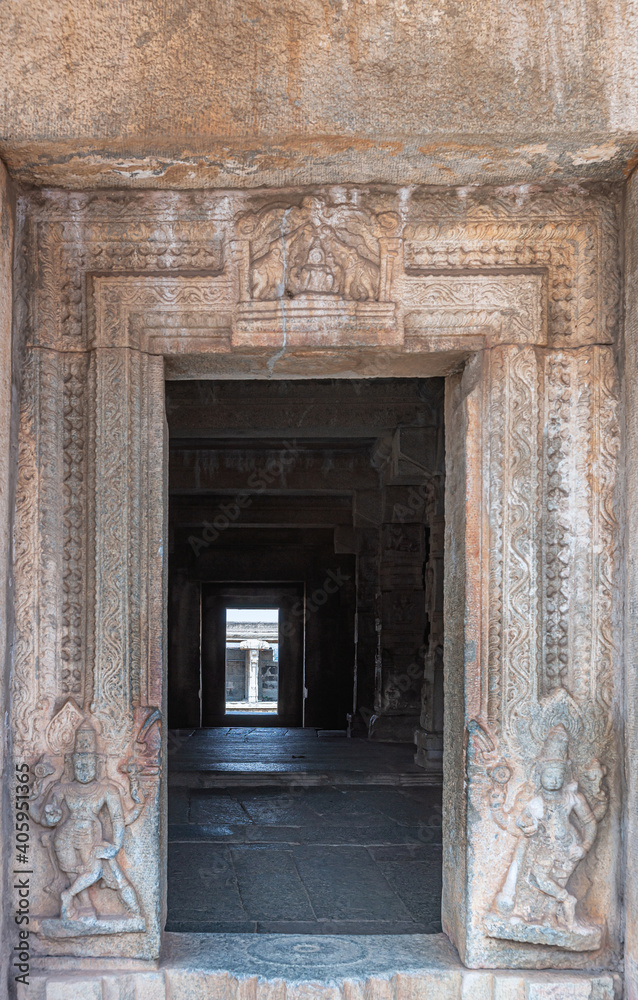 Hampi, Karnataka, India - November 5, 2013: Vijaya Vitthala Temple. Looking through the brown stone doorway into darker sanctum. Vishnu sculptures in door frame. Lakshmi fresco on top.