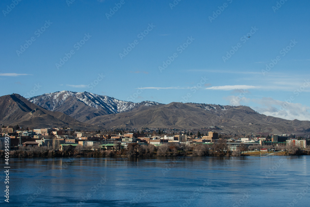 A city behind a wide river against a background of blue mountains on a sunny day against a background of a bright blue sky