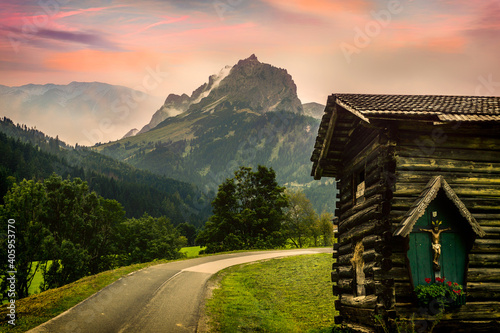 Wooden Alpine hut with a God statue and with the Alpine mountains in the background at sunset photo