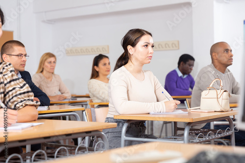 Focused young attractive brunette listening to lecture in classroom with group of adult people. Postgraduate education concept