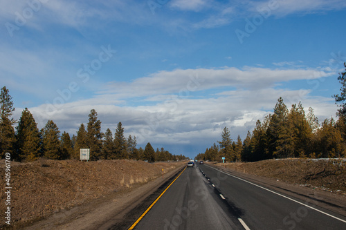 Beautiful road landscape on a sunny autumn day. A highway among tall fir trees  ahead of a beautiful cloudy gray-blue sky before the rain.