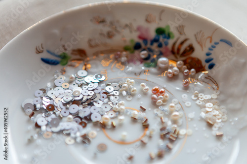 Beads, sequins, glass beads on a saucer with a painting. Close up
