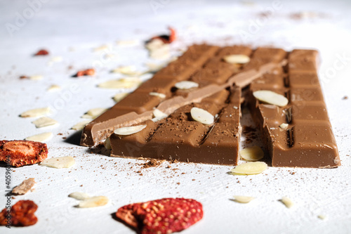 A close-up of a broken milk chocolate bar sprinkled with dried fruit and cocoa. Almond flakes and freeze-dried strawberries.