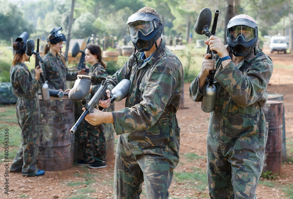 Two vigorous paintball players in full gear having fun before game outdoors
