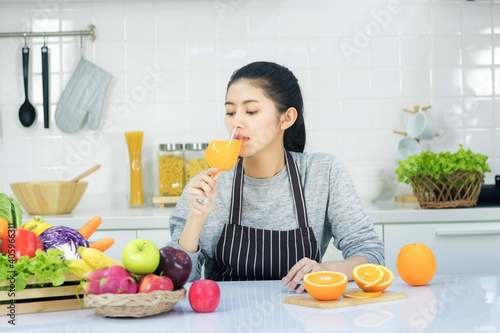 Asian women taking care of health and body shape Preparing food in the kitchen and waiting to drink orange juice in the glass.
