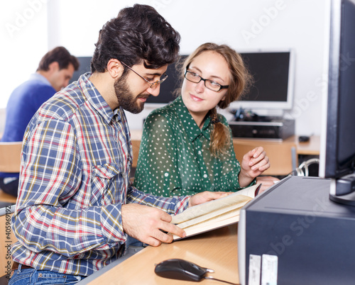 Intelligent female and male students working together with computer and book in university library ..