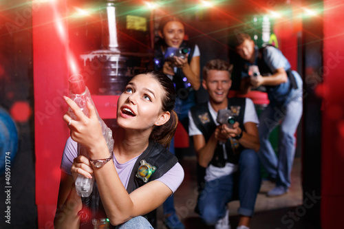 Portrait of young positive cheerful glad girl took aim colored laser guns during laser tag game in labyrinth