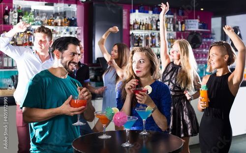 positive male with female are talking and drinking cocktails on the party in club