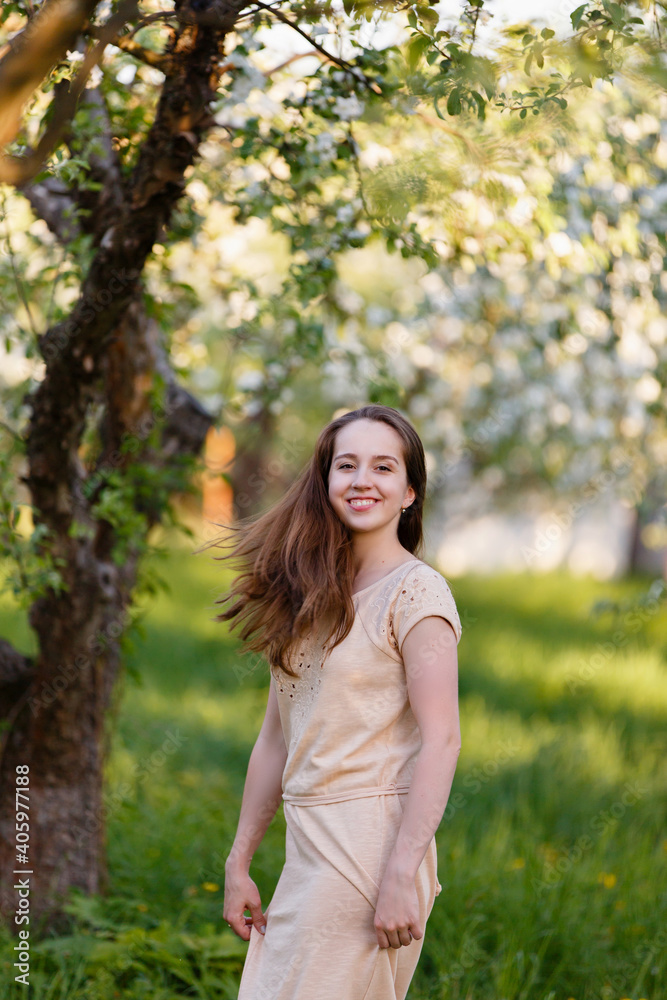 Young woman in beige dress in a blooming apple garden. Spring story. Brown-haired girl with long hairs. Woman plays with her hairs Young woman in beige dress in a blooming apple garden. Spring story. Brown-haired girl with long hairs. Woman plays with her hairs