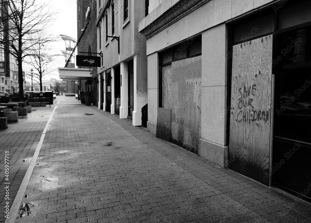 A view down a city sidewalk with boarded-up storefronts in black and white. Copy space.