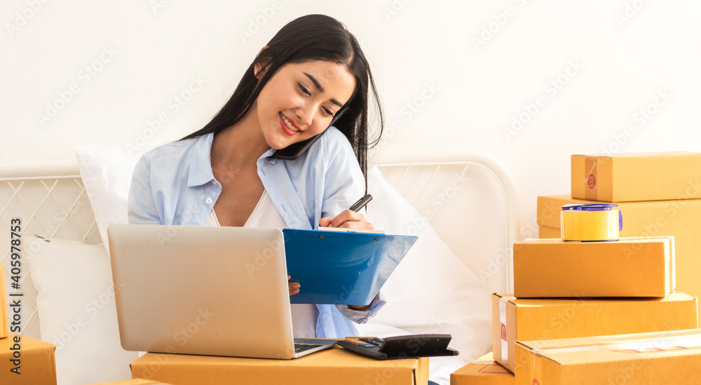 Young smiling beautiful owner asian woman freelancer sme business online shopping working on laptop computer with parcel box on bed at home - SME business online and delivery concept Young smiling beautiful owner asian woman freelancer sme business online shopping working on laptop computer with parcel box on bed at home - SME business online and delivery concept