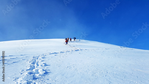 Group of people descends from the snow-covered peak of the mountain. Winter mountain tourist hiking tours.