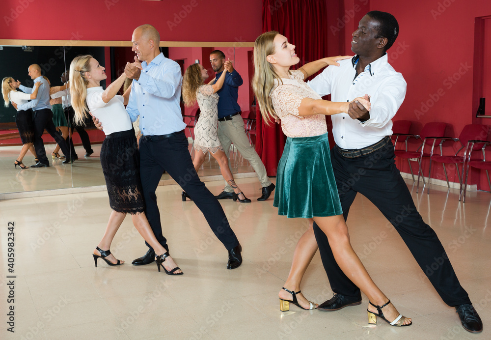 Young positive people learning to dance waltz together in dancing class