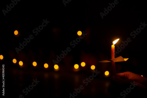 hand holding a burning candle in darkness with noise and grain effect bokeh.