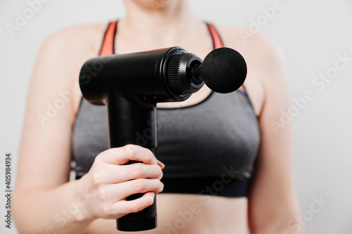 woman holds massage gun. medical-sports device helps to reduce muscle pain after training, helps to relieve fatigue, affects problem areas of body, improves condition of skin.