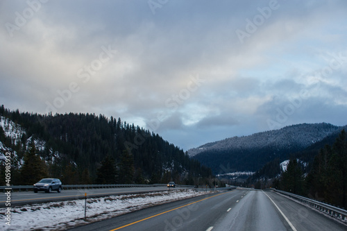 Winter Highway, on which cars and trucks travel, among the mountains covered with snow. Winter road landscape at sunset with beautiful sky of blue and pink shades. Hwy 90, Idaho, USA. 2-8-2020