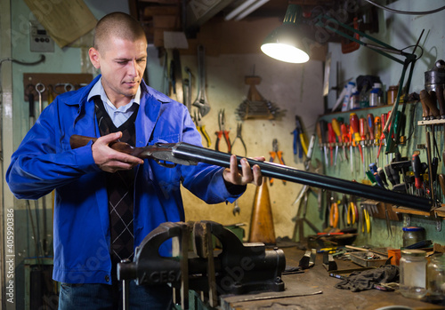 Focused master of weapon workshop inspecting semi-automatic double-barreled hunting shotgun before repair