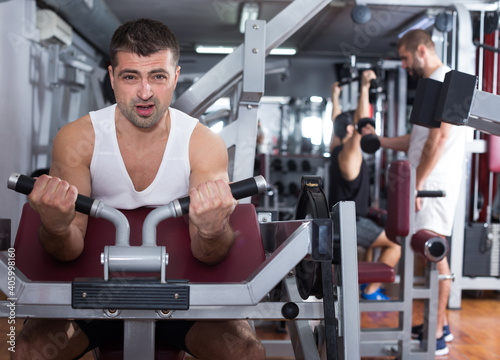 Sporty guy training muscles of arms and shoulder girdle on fitness machine in gym