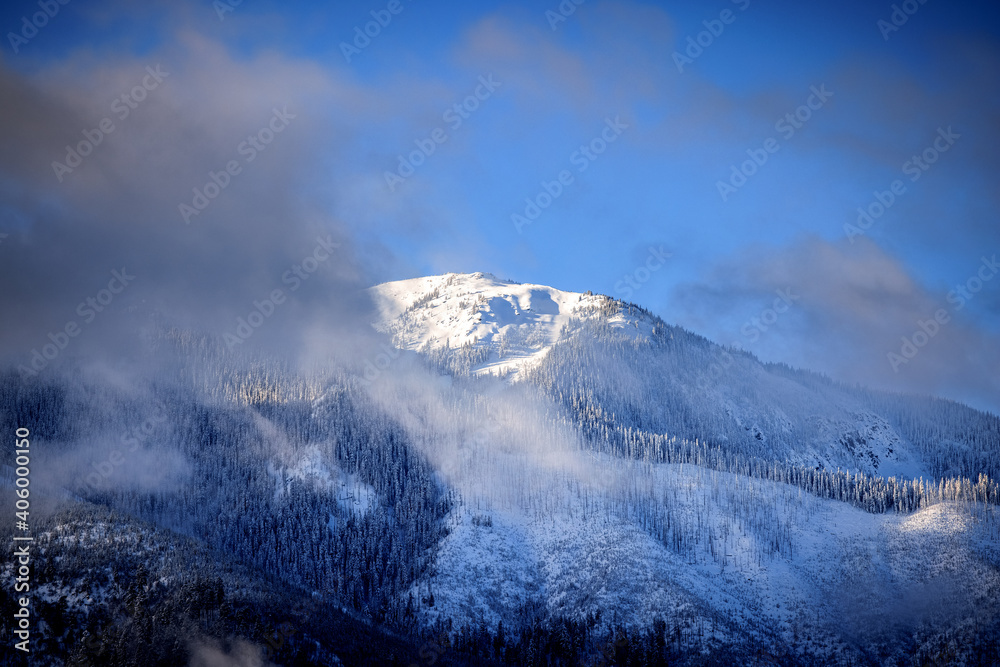 Snowy mountain peak through clouds blue sky