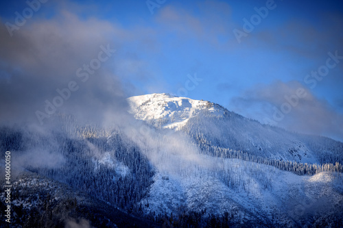 Obraz na płótnie Snowy mountain peak through clouds blue sky w salonie