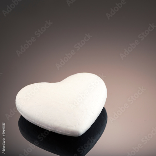 White 3d heart made of polystyrene, on a dark background with place for text. Artificial love concept, frozen heart. Studio photo. Valentine's Day. Side view