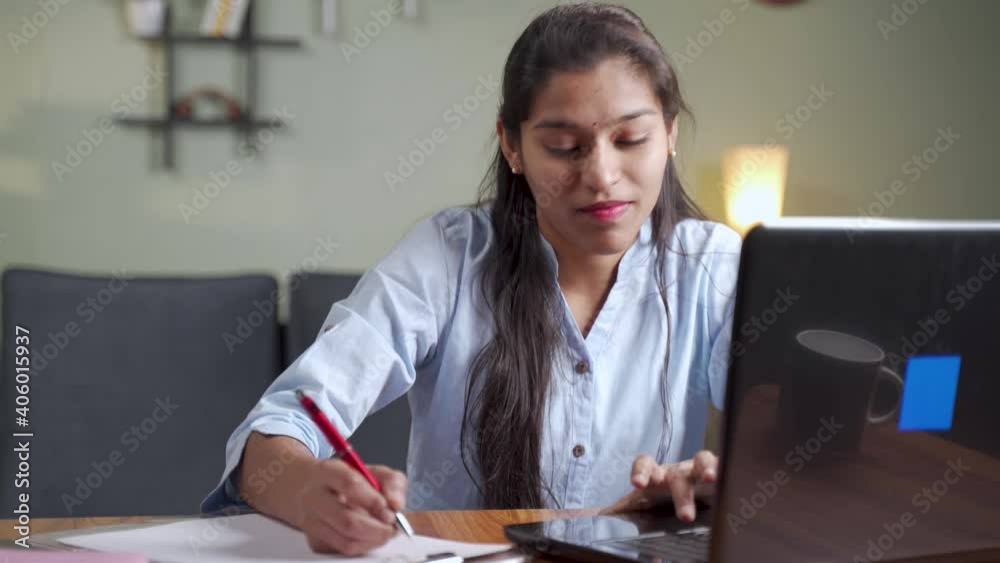 Young business woman writing down notes by looking laptop - concept of employee or student online training class at home