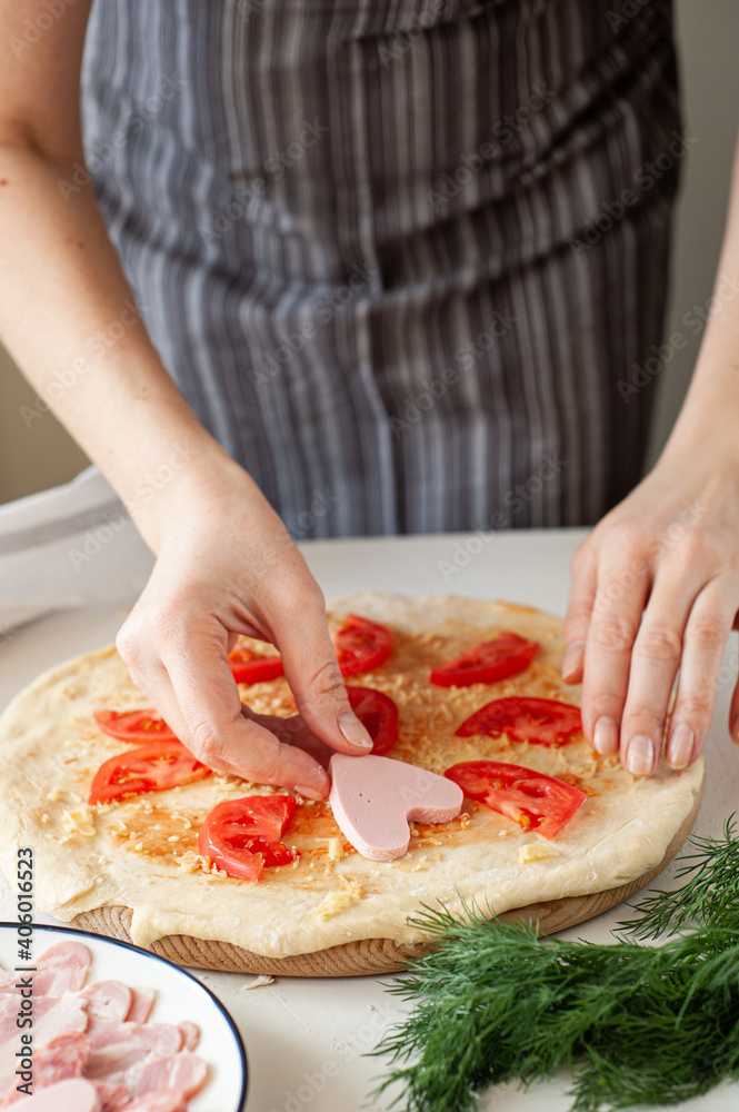The process of making homemade pizza for Valentine's Day. Women's hands lay the ingredients cut in the form of hearts on the base of the dough. The process of making homemade pizza for Valentine's Day. Women's hands lay the ingredients cut in the form of hearts on the base of the dough.