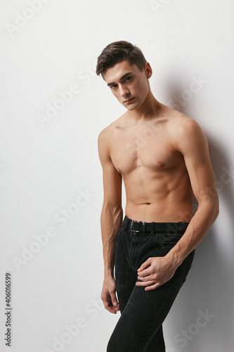 A guy with a naked torso on a light background in trousers cropped view