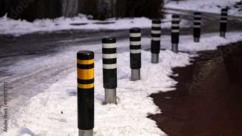 bollards with yellow and white reflect strip in the apartment complex. Snow is piled up on the ground.
