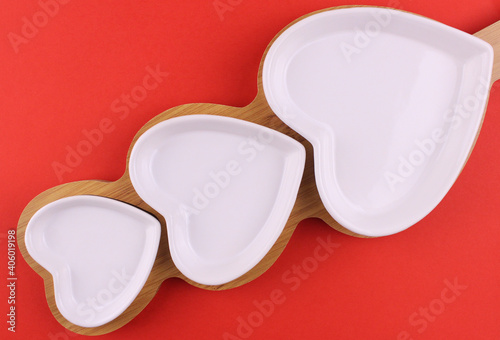 Set of white plates of different sizes in the shape of a heart on a wooden stand
