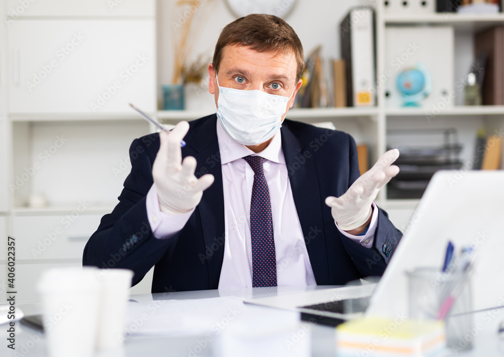 Businessman in protective mask and gloves working alone with laptop and papers in office, business process during pandemic situation