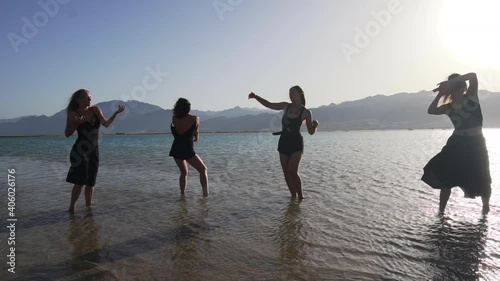group of young females dancing ecstatic in sea at sunset slow motion photo