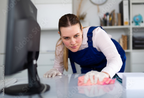 Cheerful woman professional cleaner cleaning desk with detergents in office