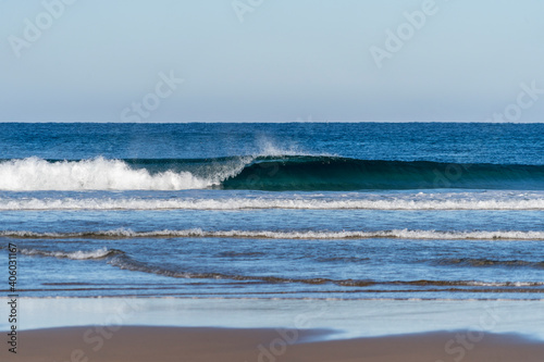 Fototapeta Naklejka Na Ścianę i Meble -  Wave breaking on a bright sunny morning. Perfect wave barrel with offshore wind on a sand beach break