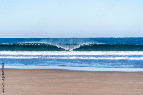 Wave breaking on a bright sunny morning. Perfect wave barrel with offshore wind on a sand beach break