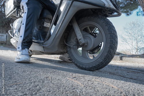 close up of a motorbike and legs of a young man delivery guy on the asphalt road low angle