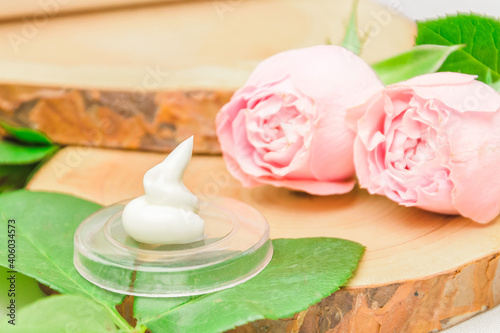 Drop of white cream with pink roses and green leaves on wood cuts. Close up. Natural cosmetic product concept, face care and skincare