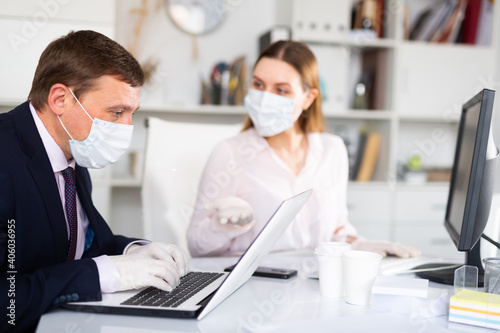 Director and secretary in protective medical masks work in the office