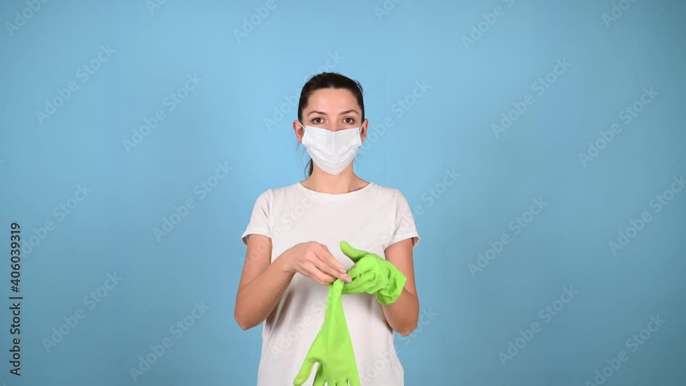 Young woman in medical mask, puts on protective green gloves, preparing for coronavirus epidemic or cleaning. Cleaning service, housekeeping concept. Young woman in medical mask, puts on protective green gloves, preparing for coronavirus epidemic or cleaning. Cleaning service, housekeeping concept.