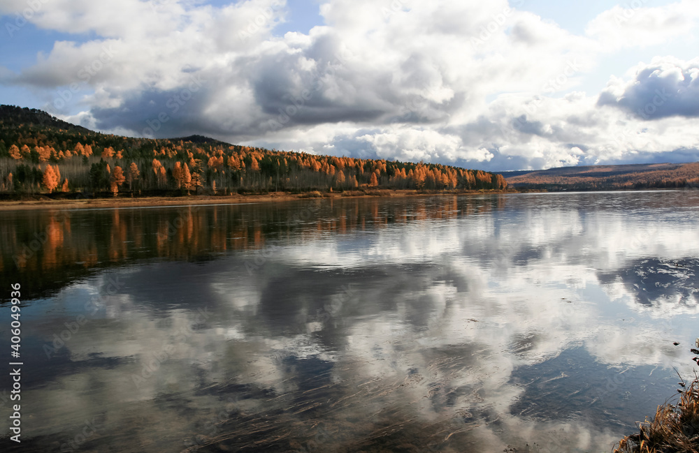 Autumn landscape on the taiga Siberian river with the reflection of the sky on the surface of clear water.